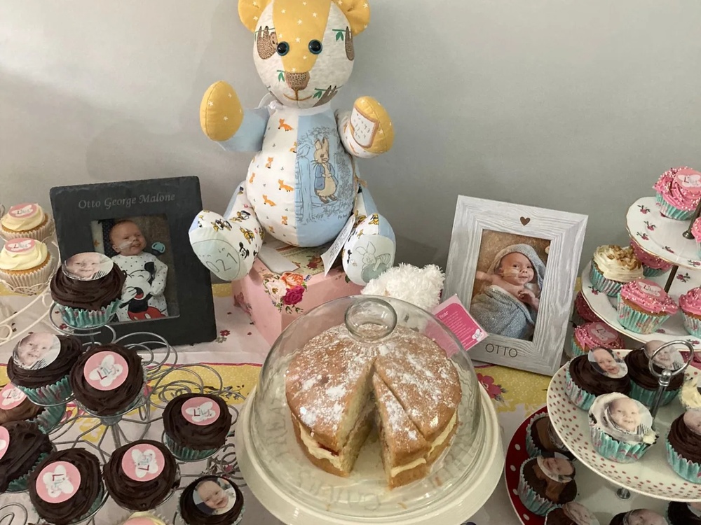 An arrangement of cakes, baby photos and a teddy bear laid out on a table