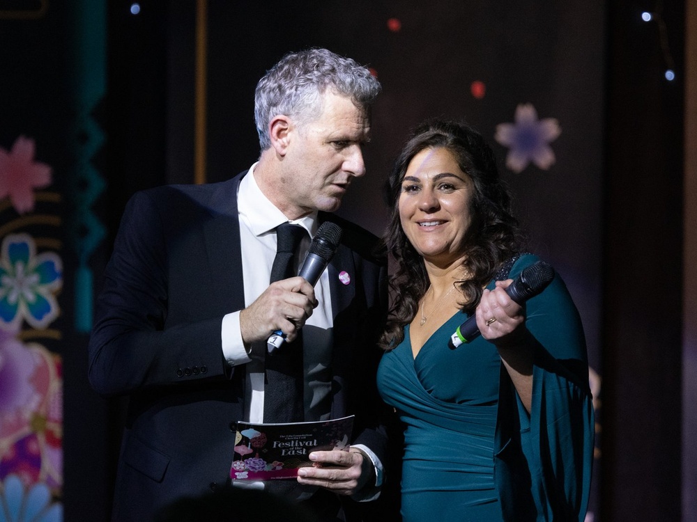Lily ball host Adam Hills on stage with charity founder Liz