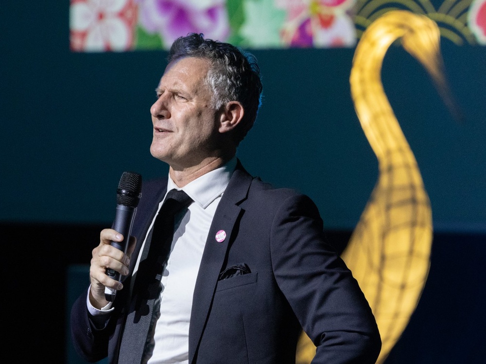 Lily ball host Adam Hills speaking into a microphone