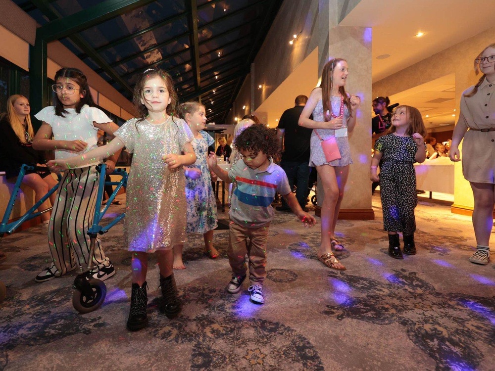 Several boys and girls of different ages are dancing in a room with disco lights