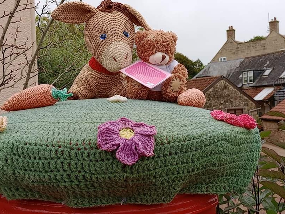 A Lily bear perched on top of a knitted novelty post box topper