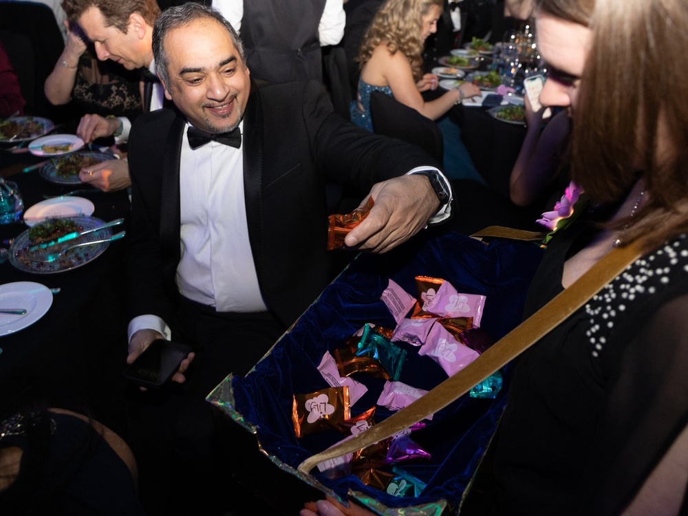 A man in a black tuxedo selects a fortune cookie raffle ticket from the basket