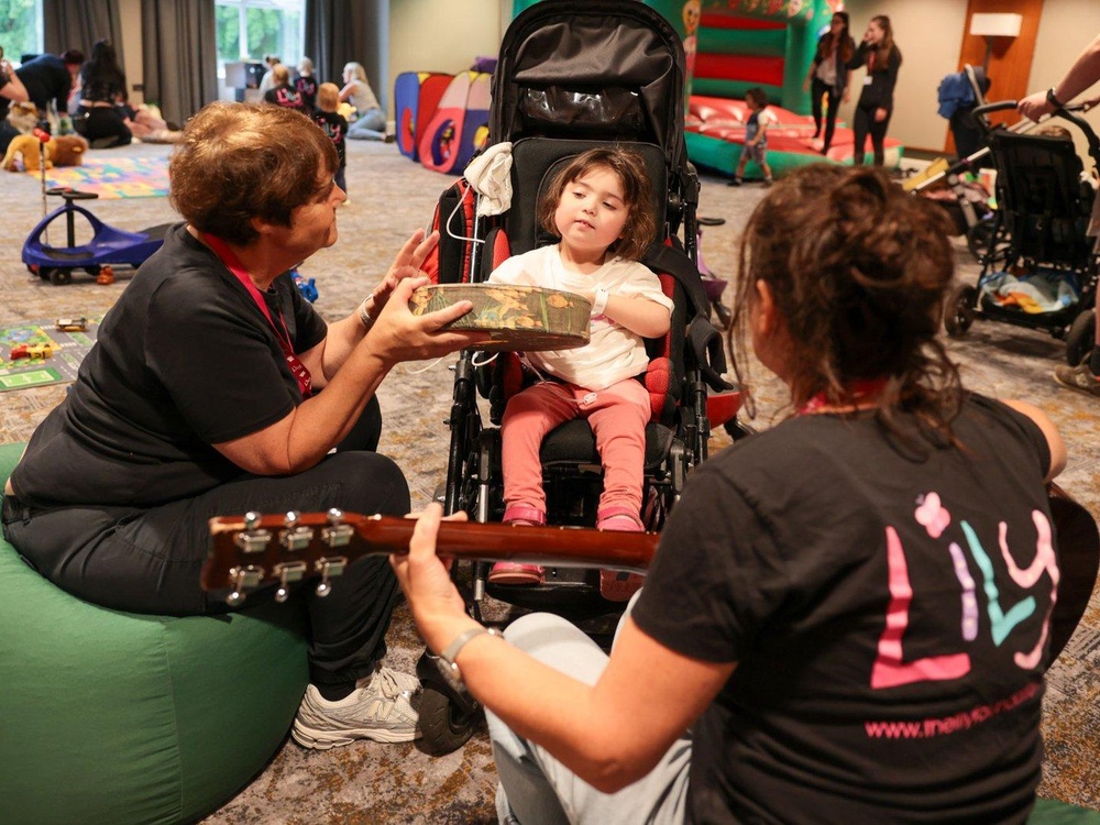 A young girl sits in a buggy while two ladies sit in front of her playing a guitar and tambourine
