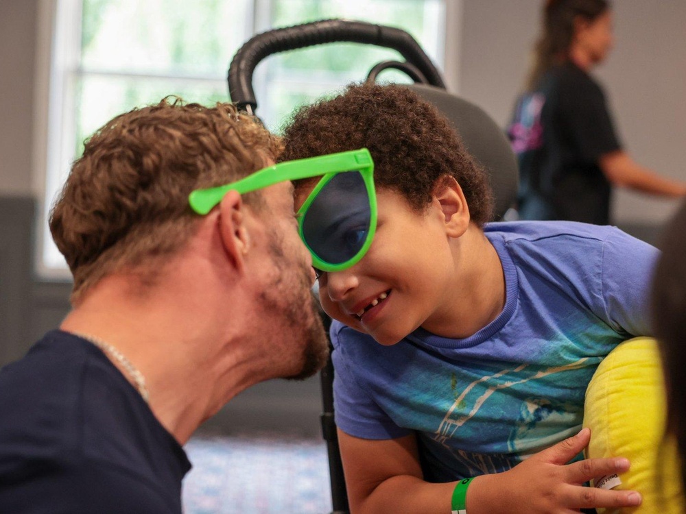 A man wearing oversized sunglasses is laughing close-up with a child
