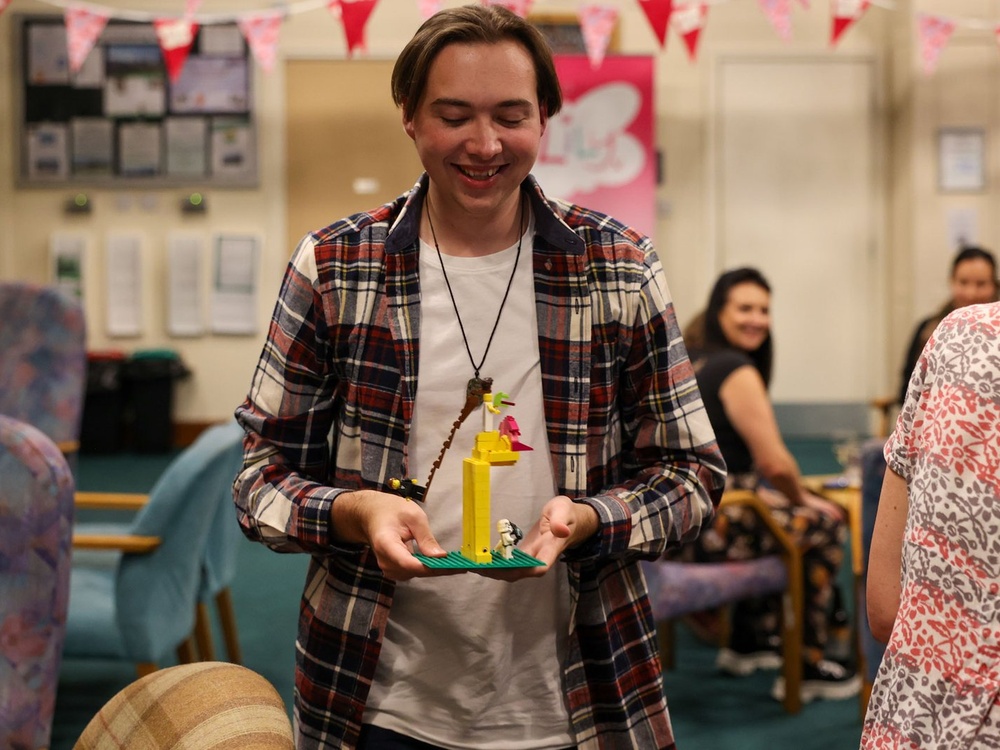 A man is carefully carrying a yellow lego model  while laughing