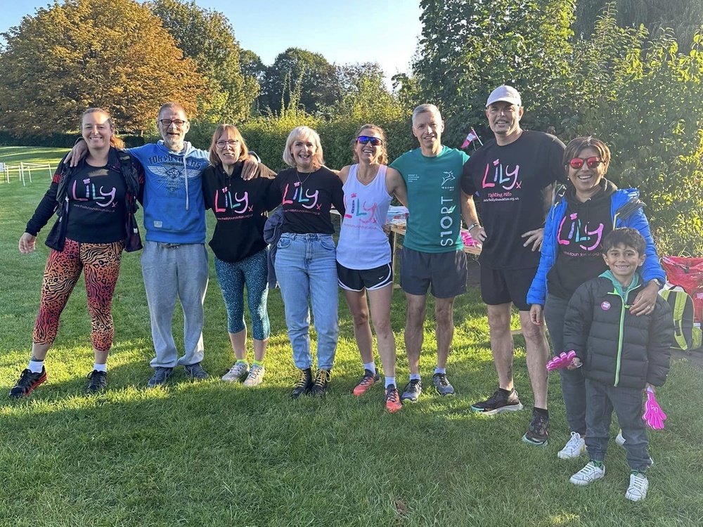A group of people, some wearing Lily tops and running gear, standing in a park with arms linked