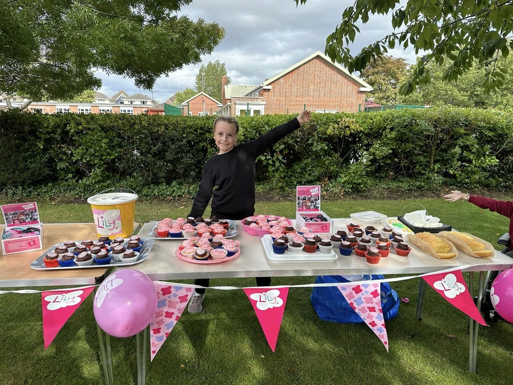 A child stands behind a table filled with cakes and bakes and hug with Lily bunting and balloons