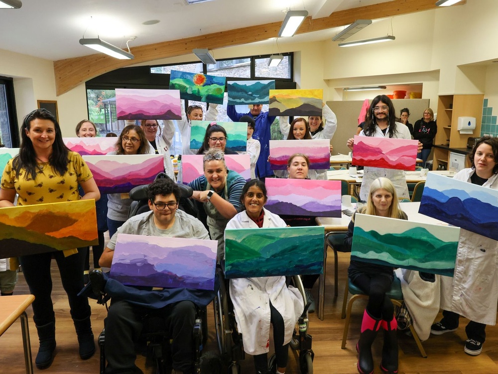 A group of people seated and standing are holding up colourful canvases