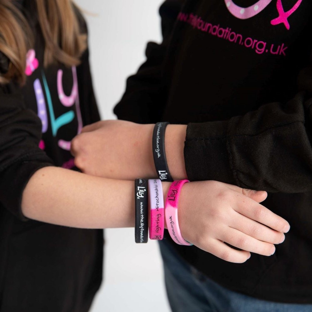 Two people holding their wrists together, both wearing wristbands featuring the Lily Foundation logo