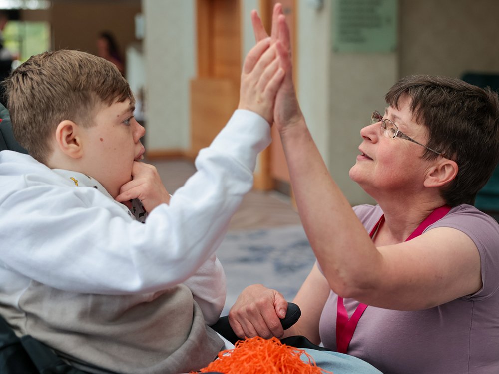 Carer high fiving a mito patient in his wheelchair