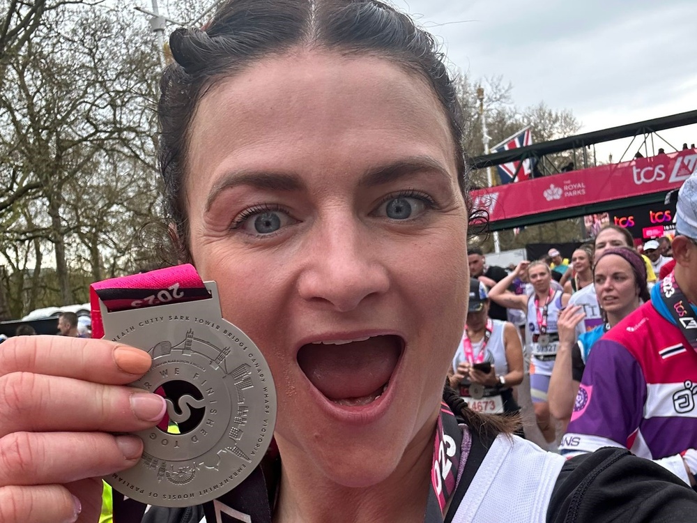 A lady smiles and holds her London marathon finishers medal up near her face