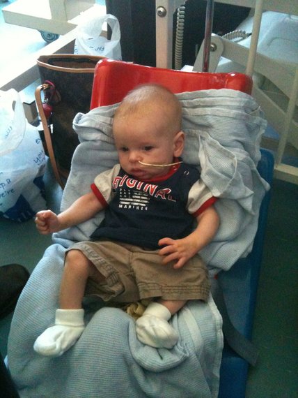 A baby with mitochondrial disease sat in a red Tumble form seat with a feeing tube in their nose