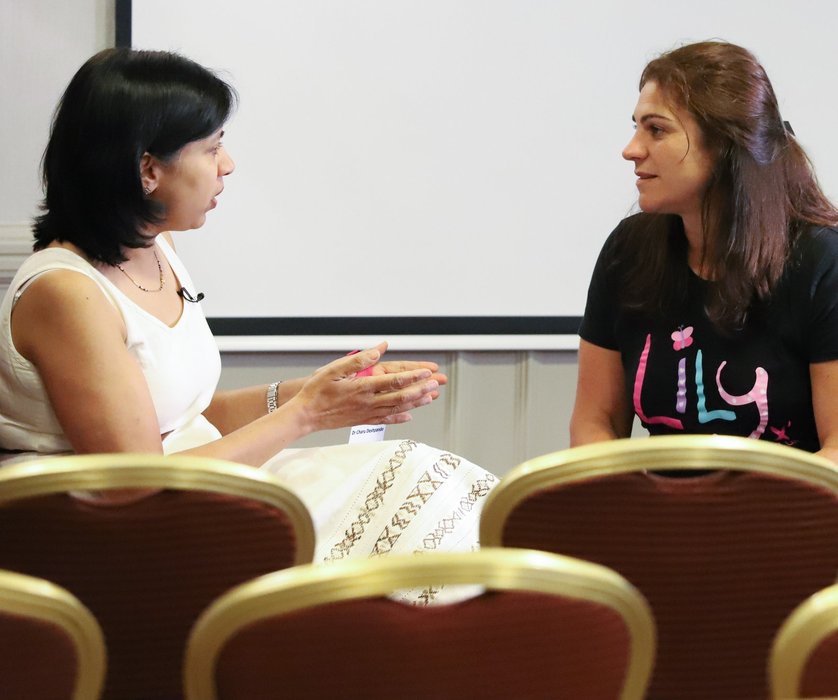 two women sitting on chairs facing each other deep in conversation. One is wearing a Lily Foundation t-shirt