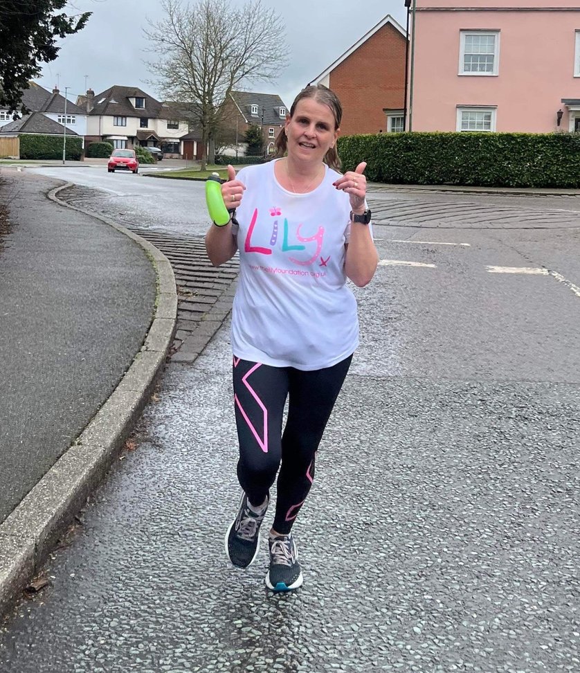 A women running in a Lily Foundation Running Tshirt with her thumbs up looking into the camera 