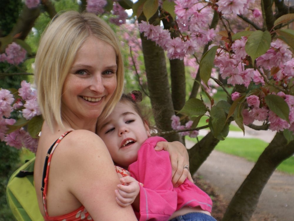 A lady holds her young daughter who has mito, standing beneath a blossom tree
