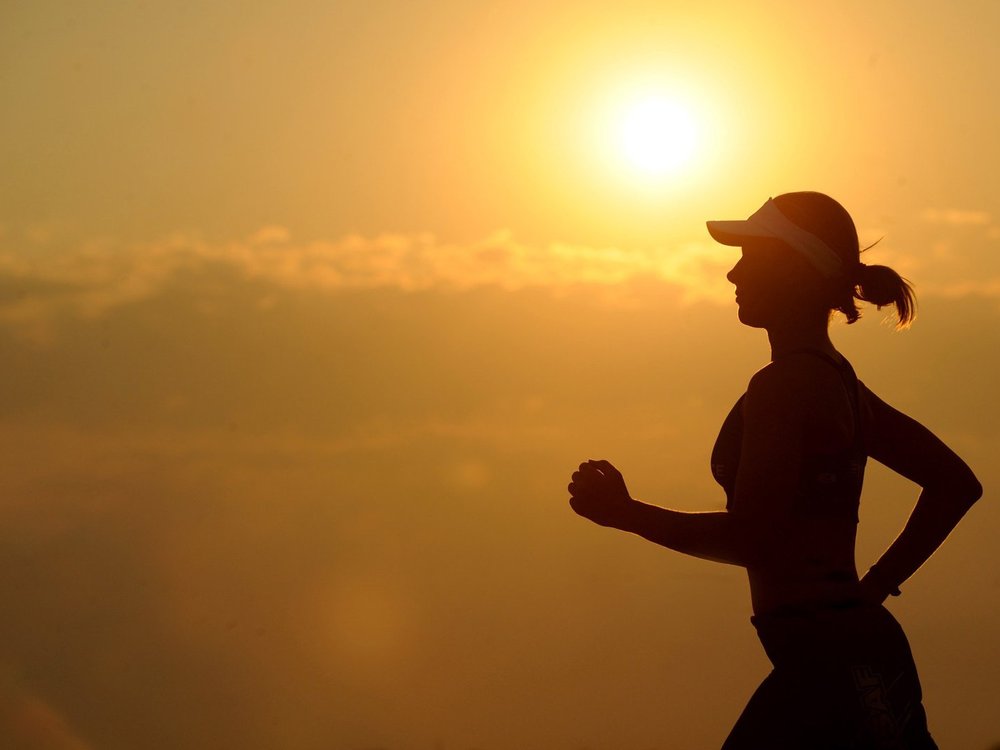 A silhouette of a women running In front of the sun