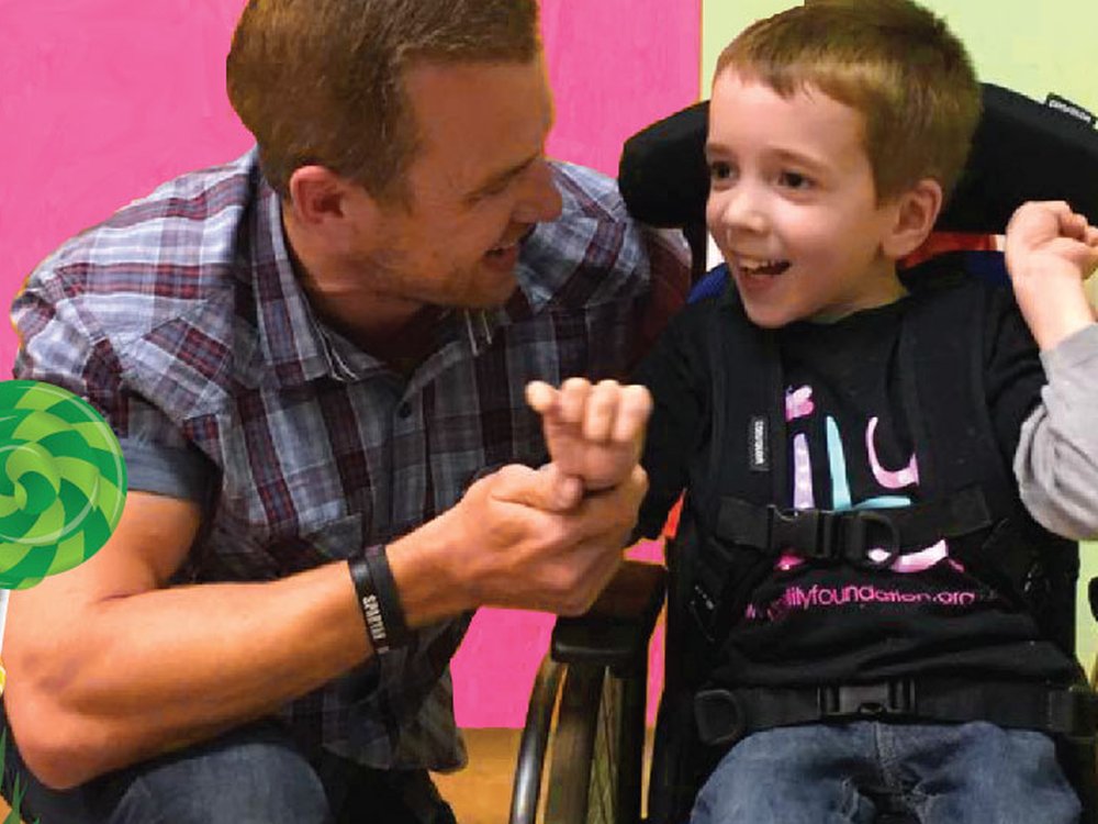 A man crouches next to a little boy with mitochondrial disease in a wheelchair