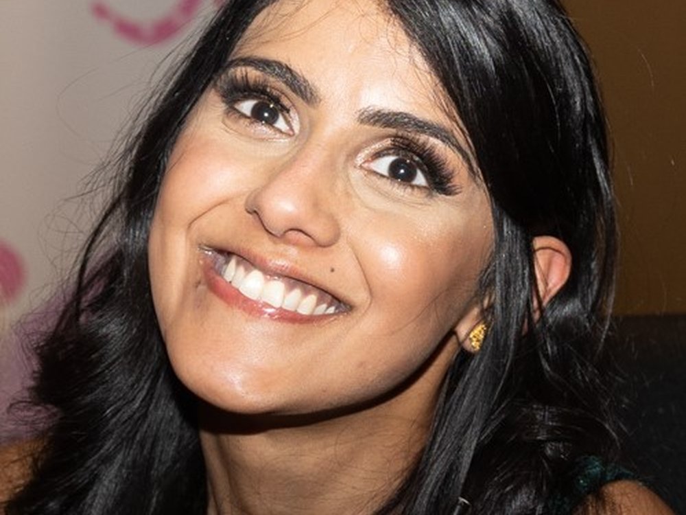 A woman with long dark shiny hair looks at the camera smiling