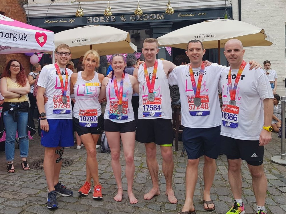 6 runners in Lily Foundation tshirts stand next to each other linking arms wearing London Marathon Medals