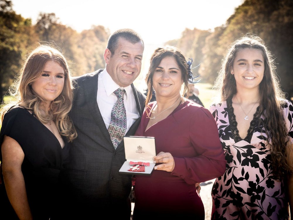 A woman hold an MBE is a presentation box. beside her are a man and two young women they are dressed smartly and smiling