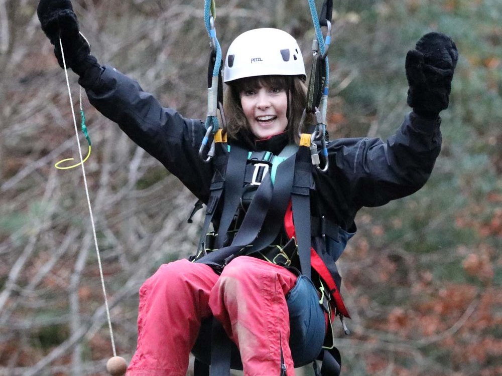 A girl in a climbing harness and helmet is suspended in the air