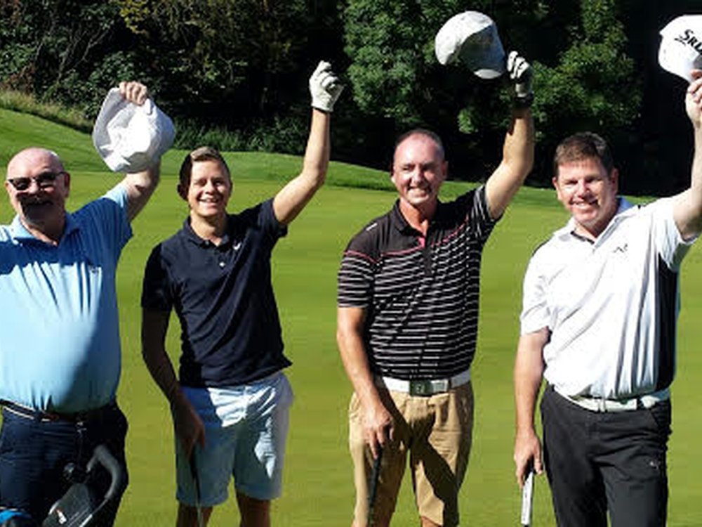four men holding golf clubs in one hand hold their other hands in the air