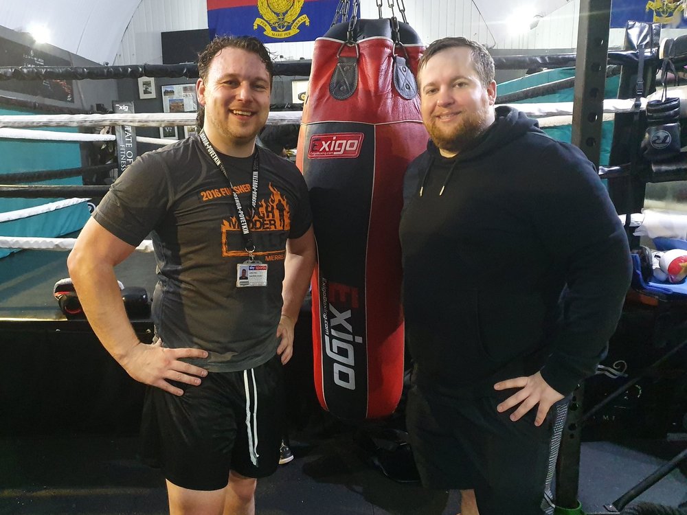 Two men standing side by side hands on hips with a punchbag between them