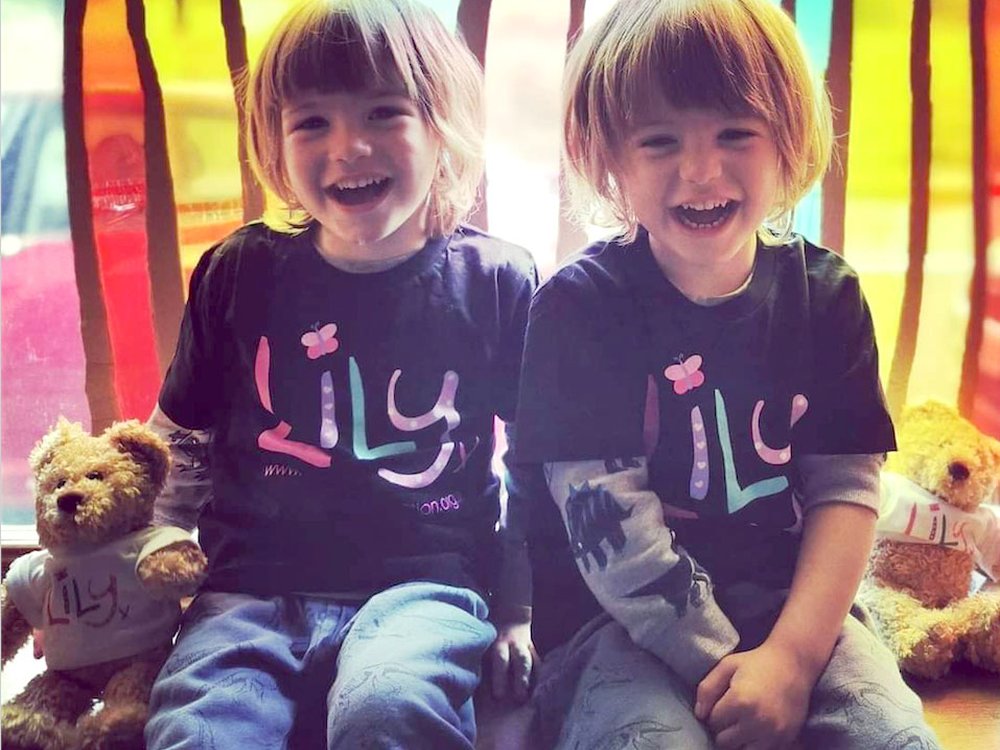 Two little boys sitting next to each other smiling at the camera wearing Lily Foundation Tshirts