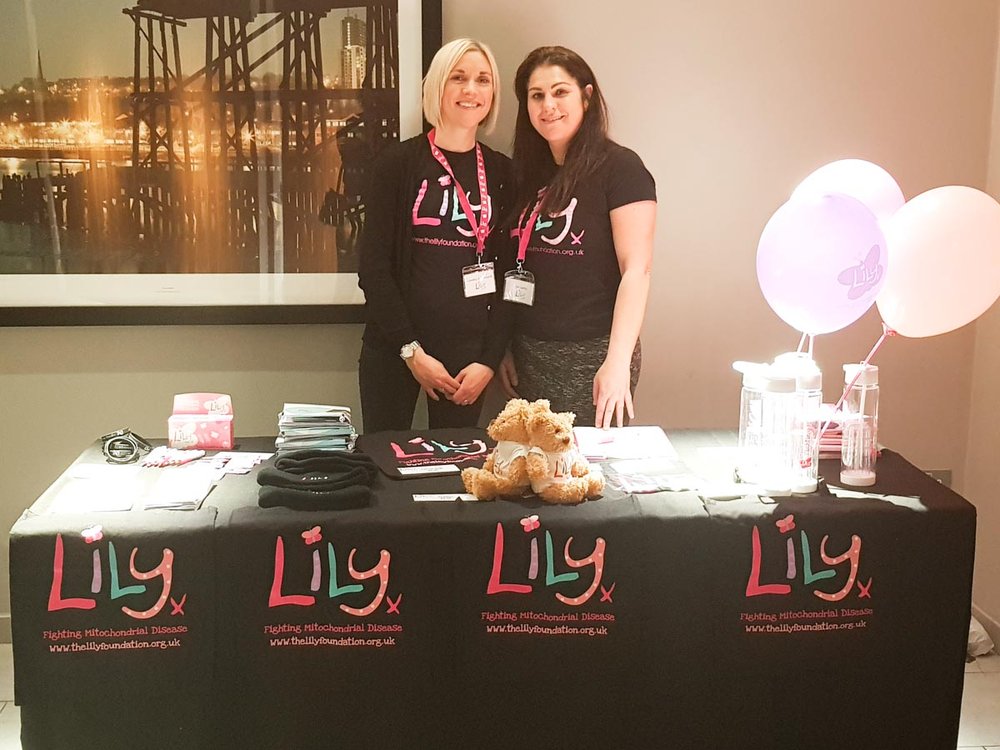 Two member of lily staff in Lily Foundation tshirts stand behind an awareness table