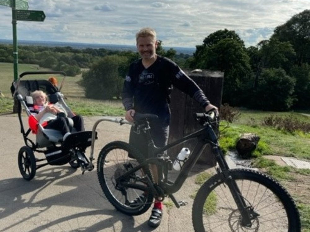 A man stood by a mountain bike. He is towing a buggy which has a young girl sat in it