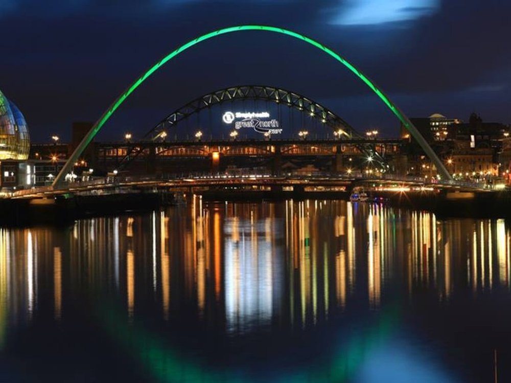 A big bridge lit up green over a large river at night