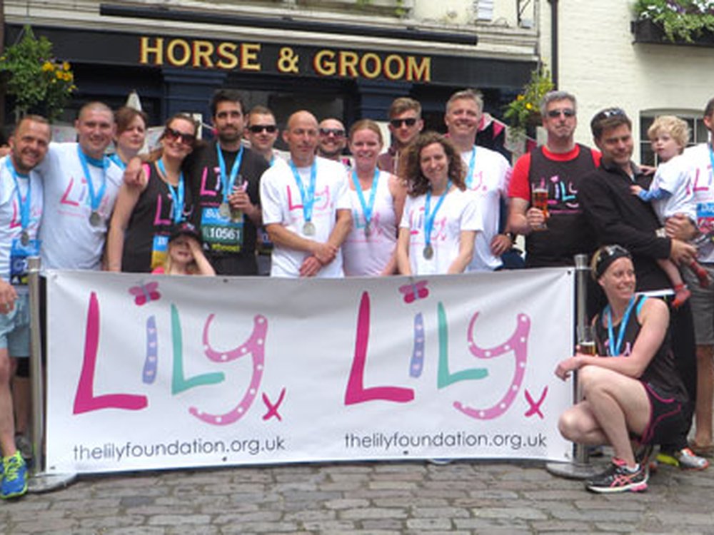 A group of people, some wearing Lily Foundation tops, standing outside the Horse and Groom pub behind a large Lily banner