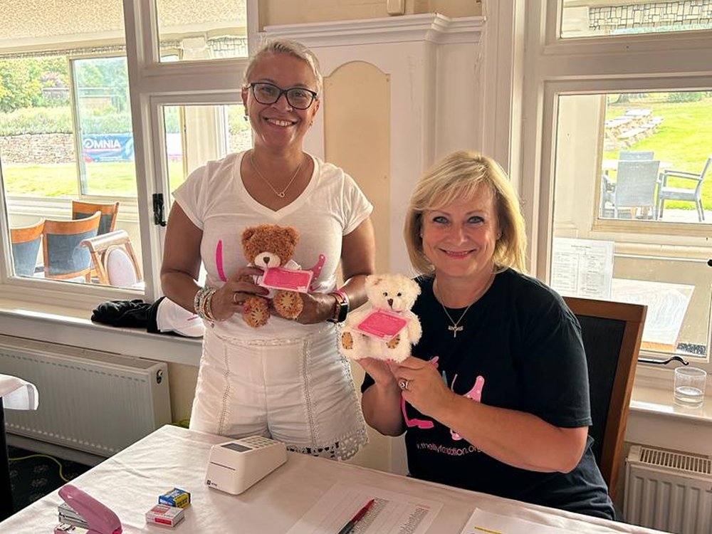 2 ladies in Lily-branded t-shirts behind a desk holding a teddy bear