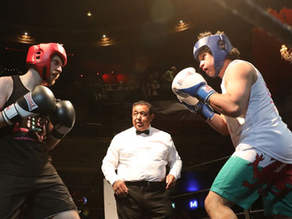 Two men sparring in a boxing ring with the referee behind