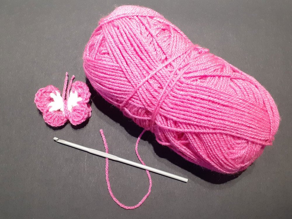 A ball of pink wool and a chochet needle with a knitted pink butterfly