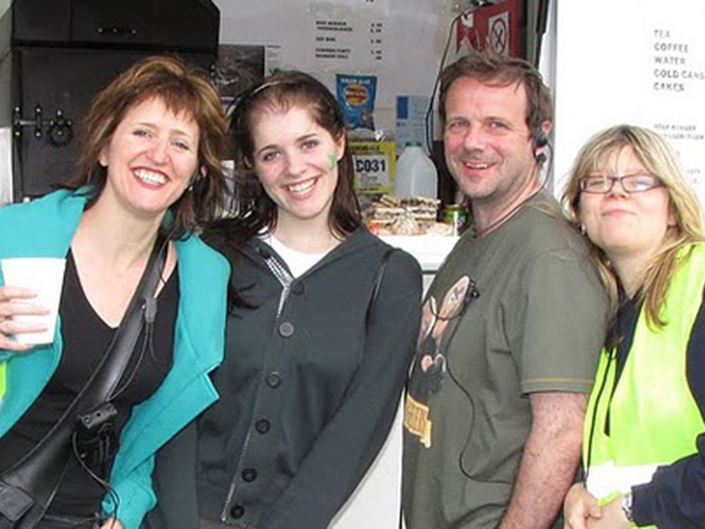 Four people leaning together and standing in front of a coffee stall smiling