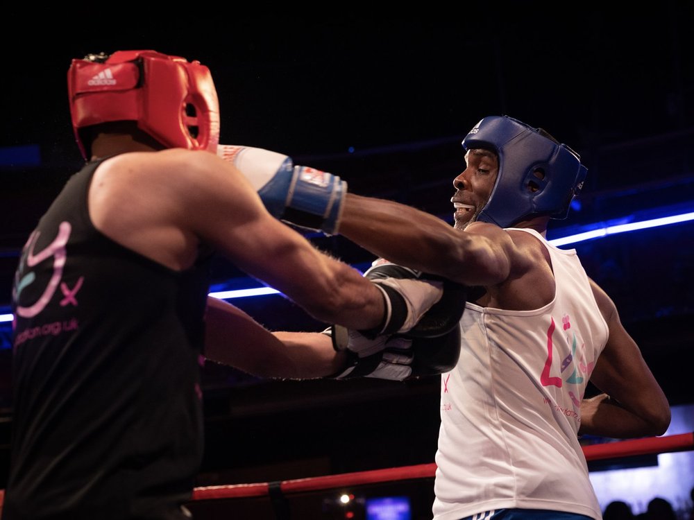 Two men in a boxing ring wearing boxing gloves, headgear and Lily Foundation vests and throwing punches at each other