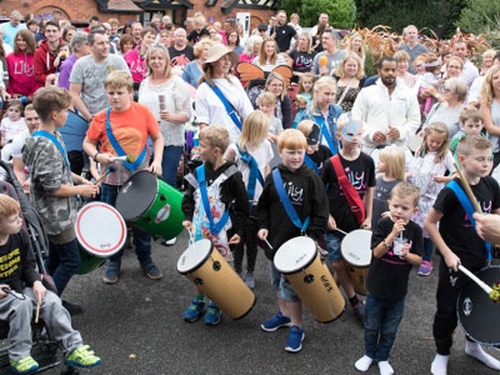Group of people gathered together at the Lily Foundation family weekend, with some children banging drums