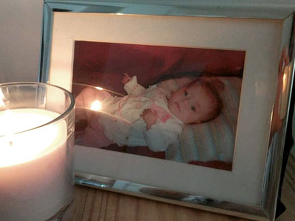 A framed photograph of a baby lying down with a votive candle burning in front of it