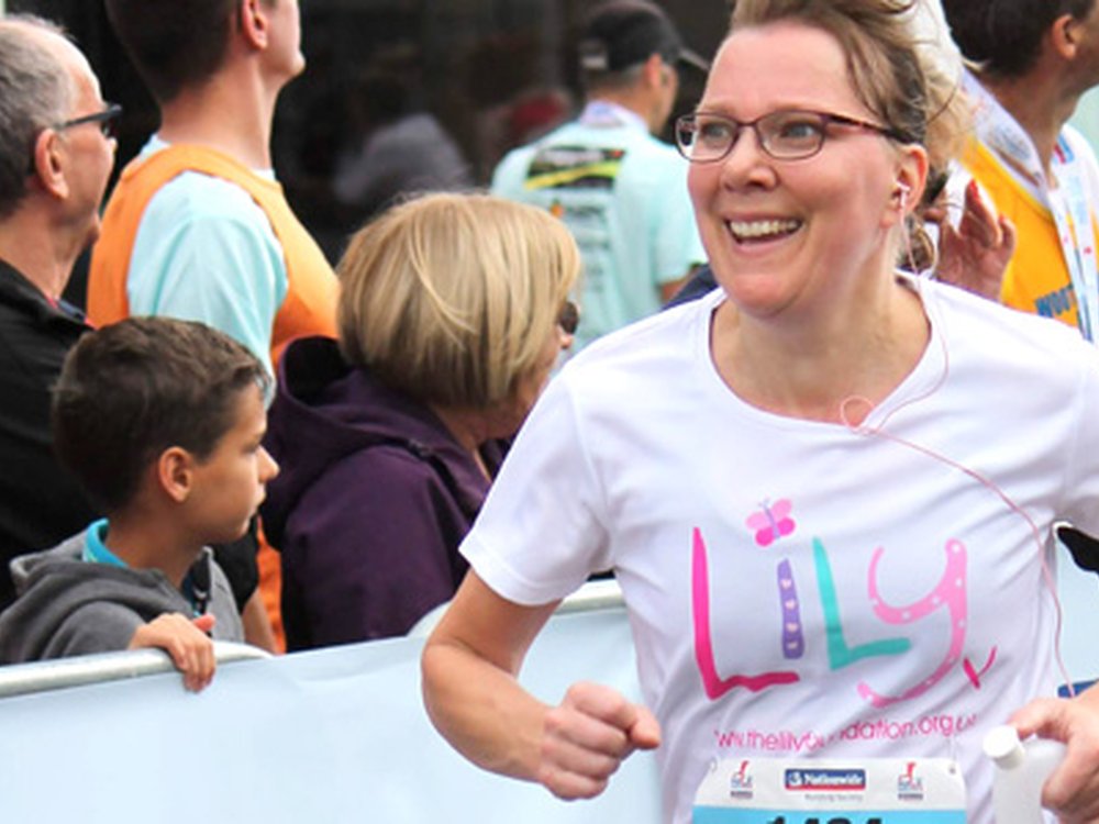 A lady in a white Lily Foundation t-shirt running past spectators and smiling