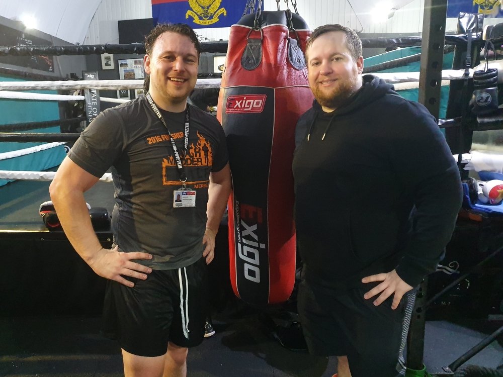 Two men standing side by side hands on hips with a punchbag between them