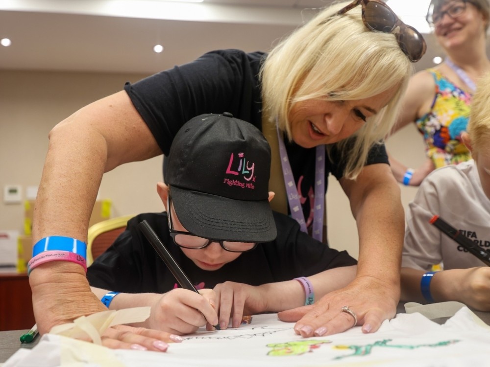 A Lily volunteer leans over a young child taking part in a crafting activity