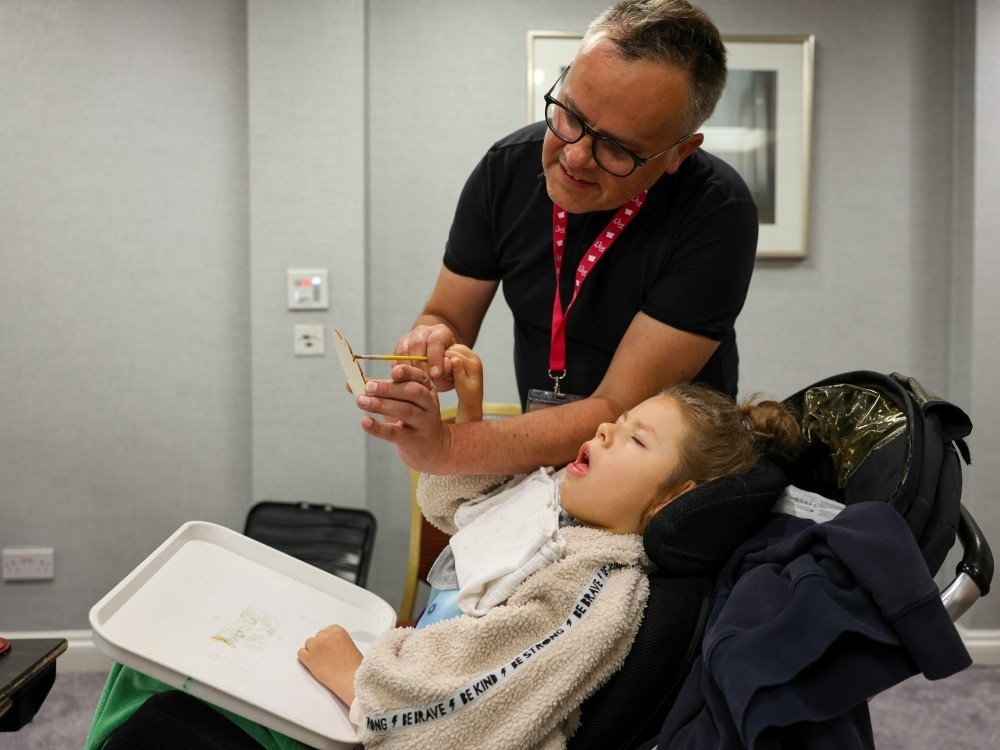 A volunteer in a Lily top leans over a young mito patient in a wheelchair