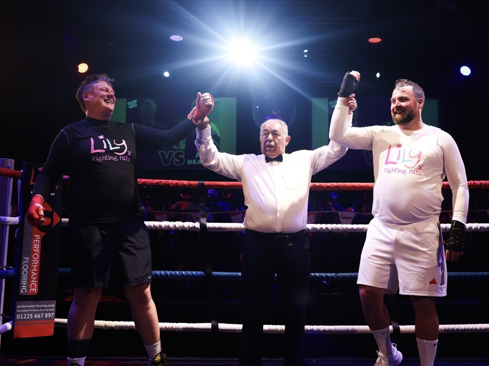 Two Lily Fight Night boxers standing either side of the ref with their arms raised