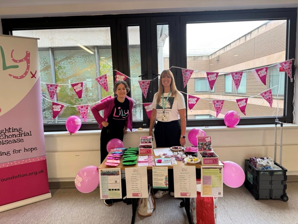 Two members of the Oxford mito team standing behind a table with bunting, balloons and Lily mrechandise to raise awareness