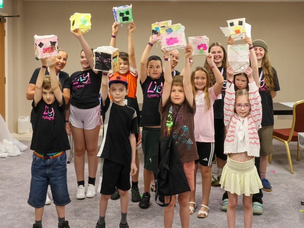 A group of young children at the Lily support weekend hold their drawings up above their heads