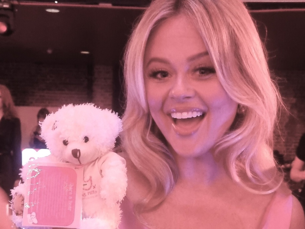 A lady holding a Lily-branded teddy bear and smiling