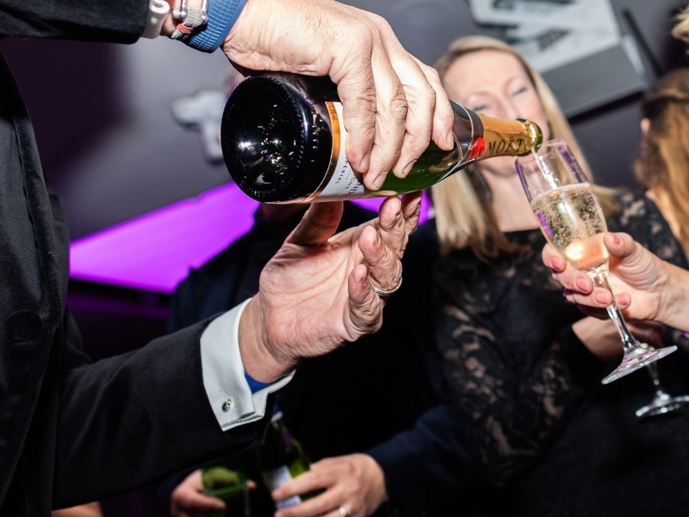 Close-up of a man pouring champagne into a guest's glass at the Lily ball