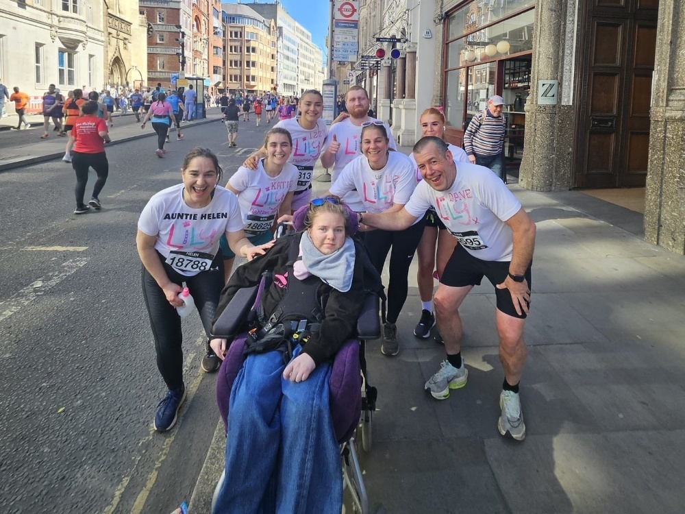 A group of supporters in Lily running tops gather around a child with mito in a wheelchair