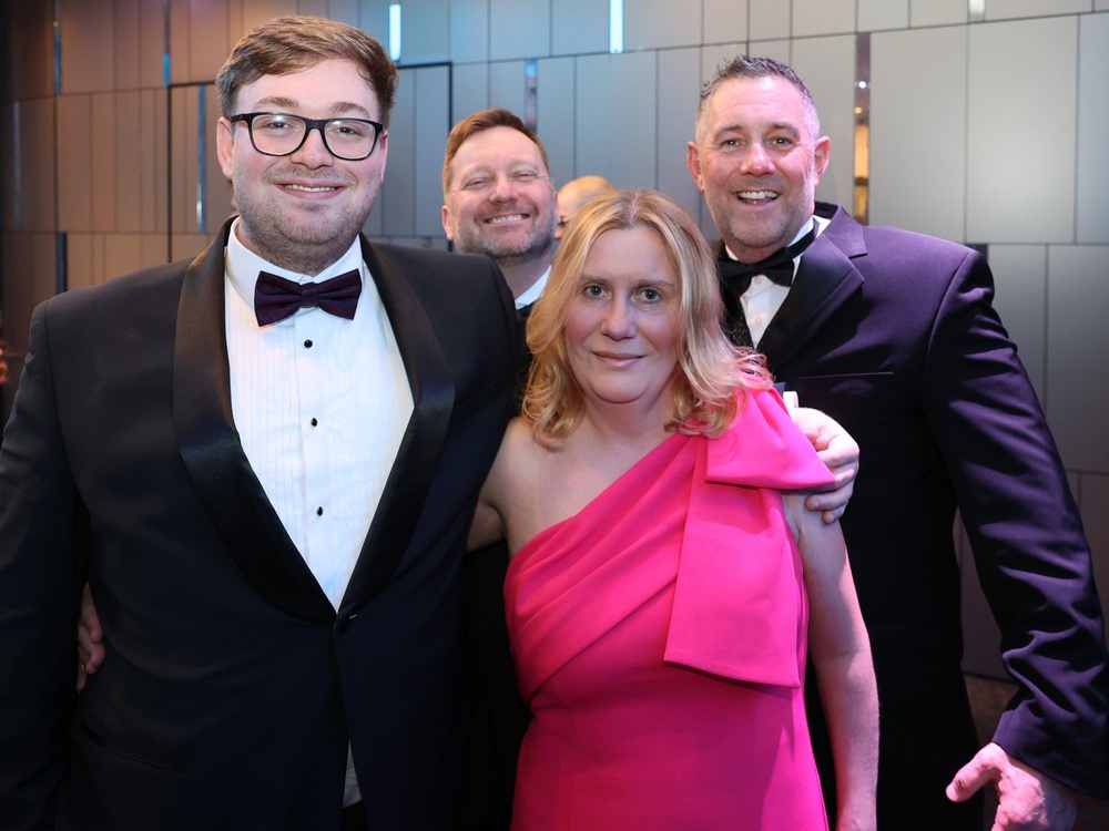 A group of people attending the Lily charity ball , the men are wearing black tuxedos and the lady a bright pink party dress